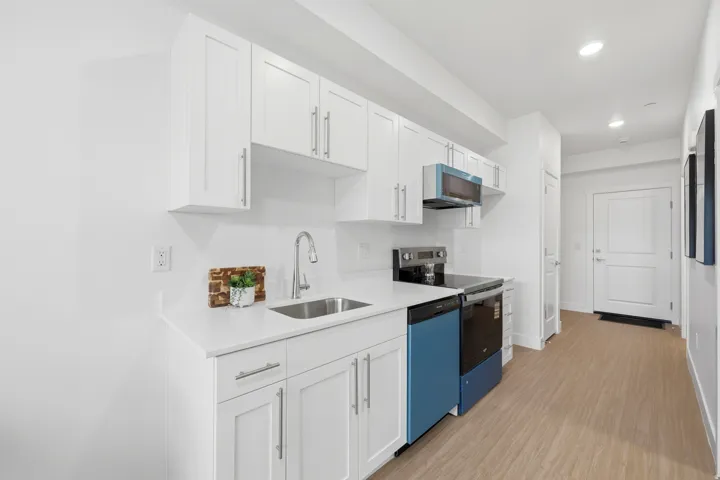 White shaker cabinetry, light-toned wood-finish flooring, stainless steel sink, sleek countertop, and integrated appliances