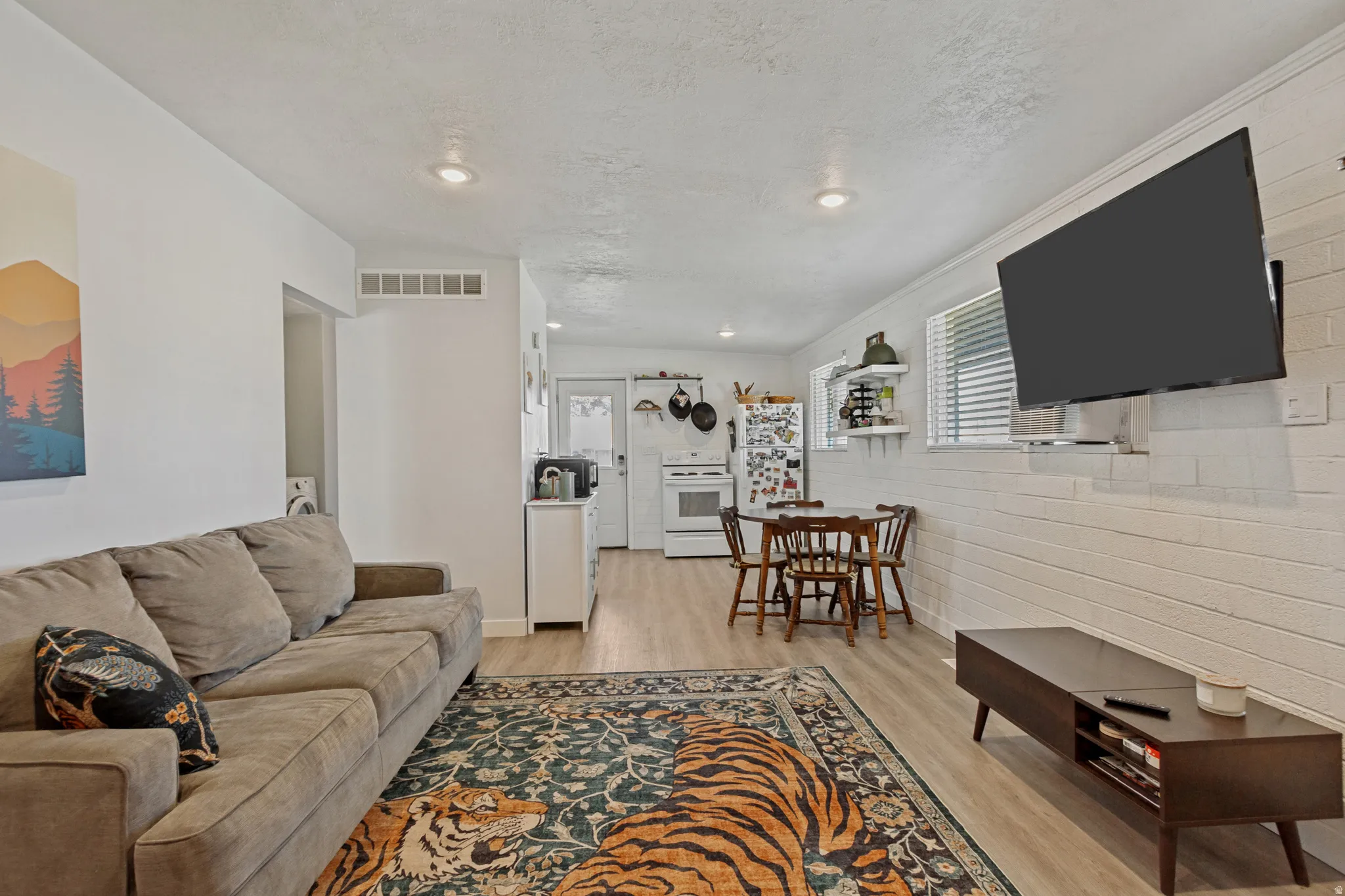 Open-concept living space featuring wood-finish flooring, recessed lighting, and white brick-style wall accents