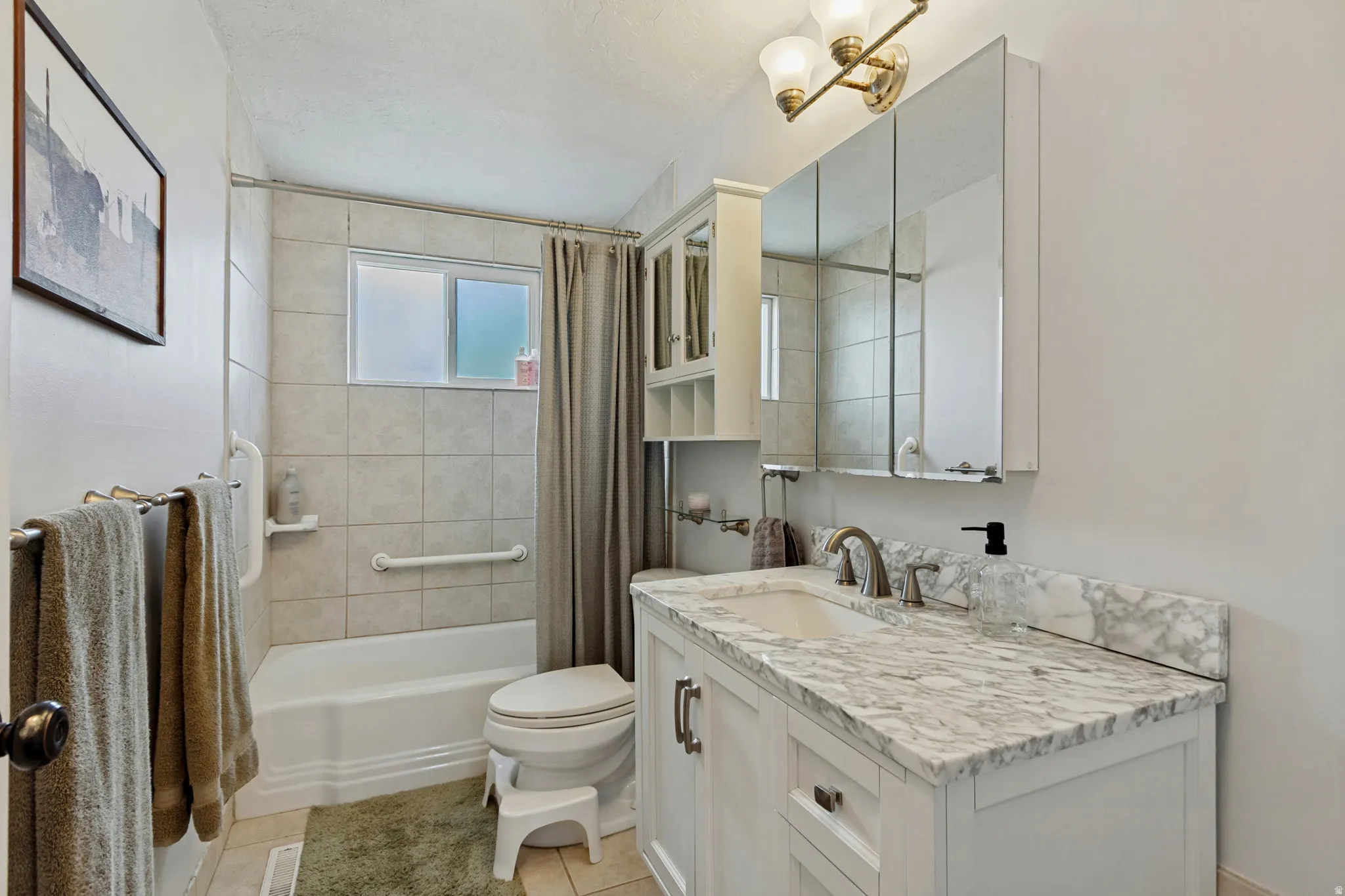White vanity with a light-toned countertop and integrated sink, dual mirrored medicine cabinet, and a bathtub with tiled surround