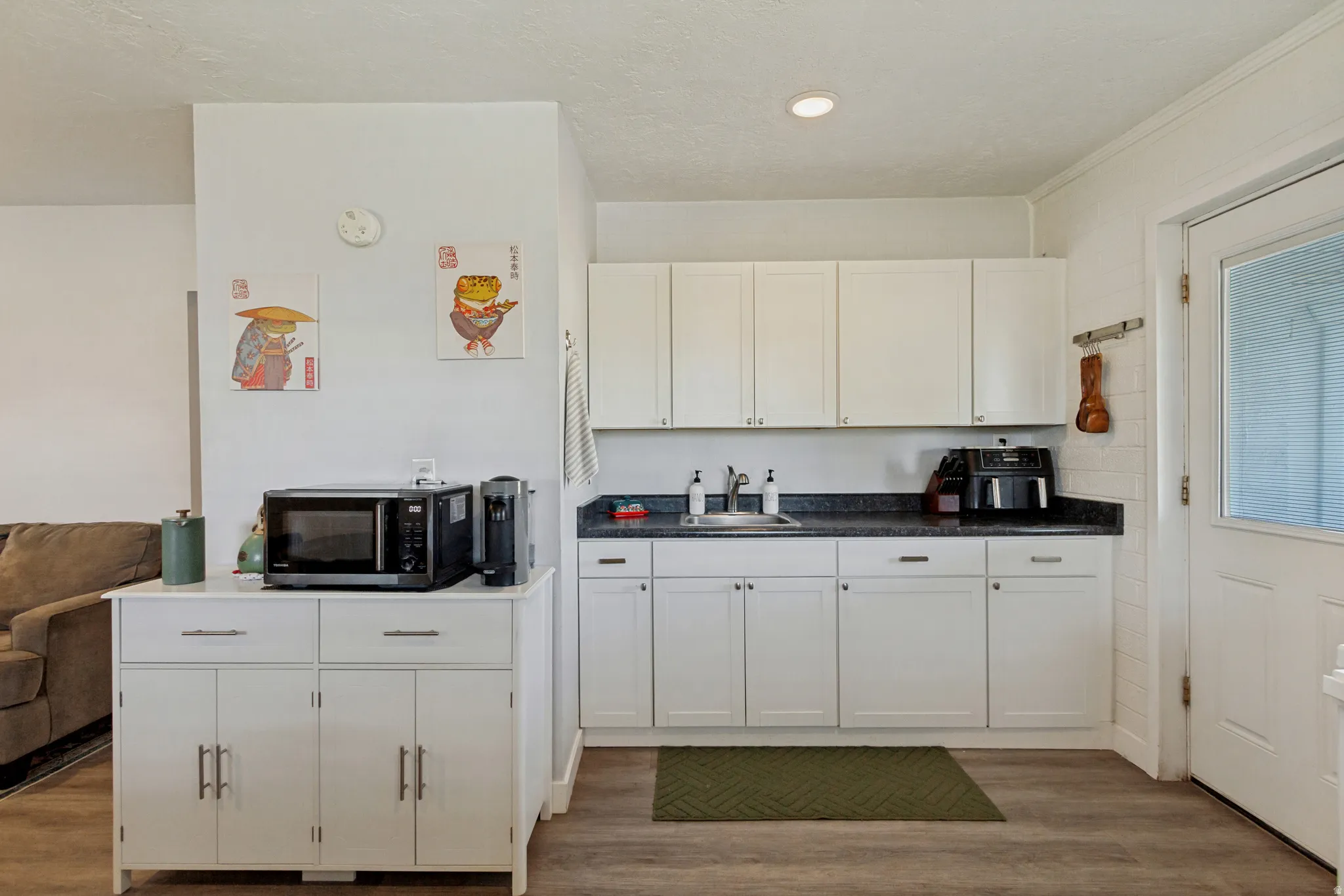 White cabinetry with dark countertops, a single basin sink, and wood-finish flooring