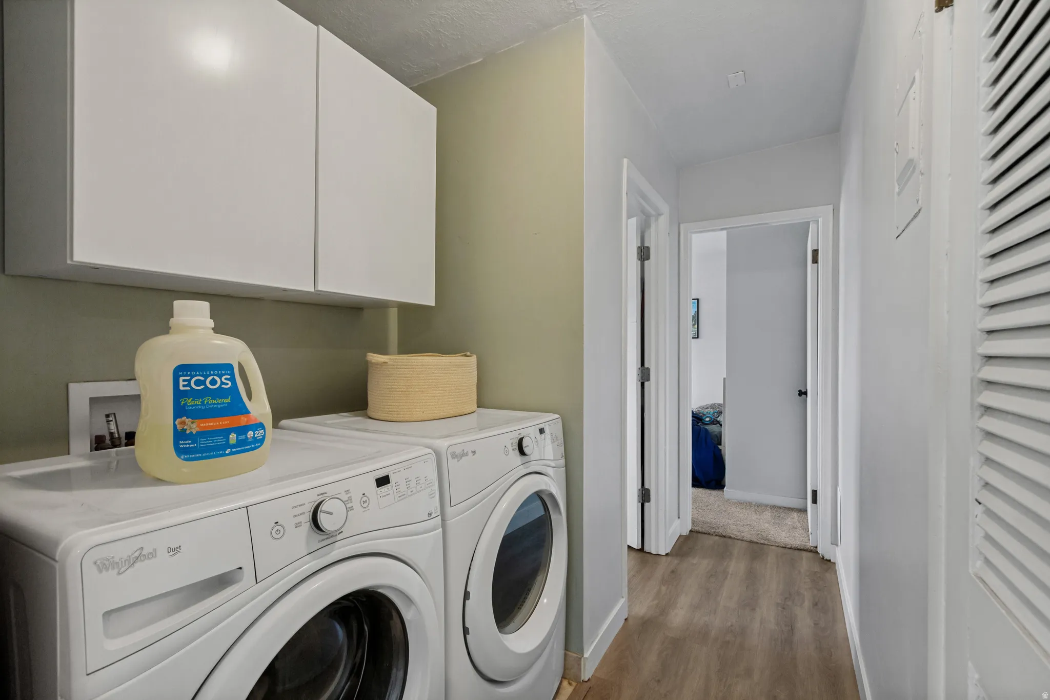 Laundry area with white upper cabinetry and wood-finish flooring