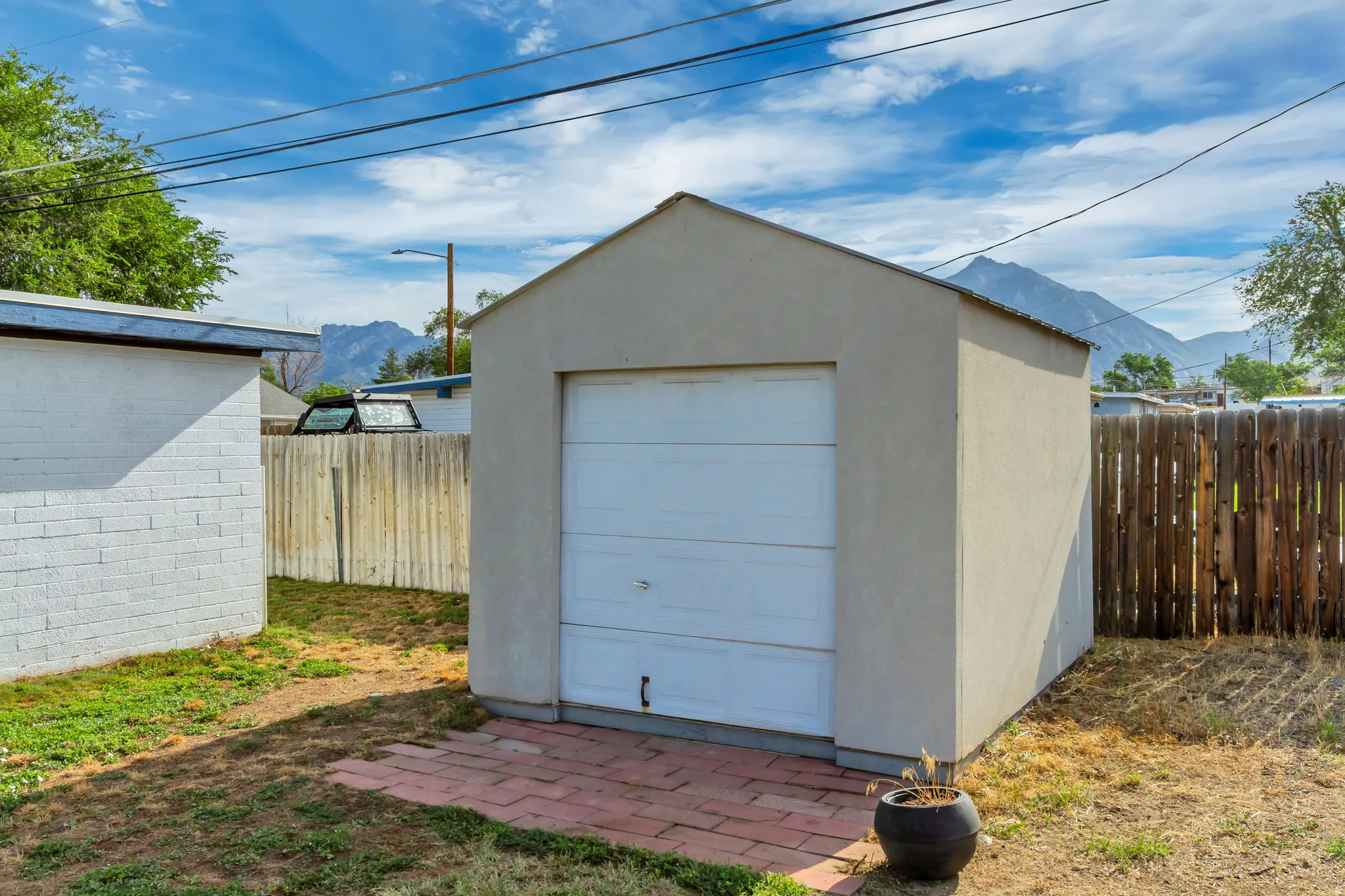 Detached storage building featuring a roll-up door, stucco exterior, and red brick paver pad