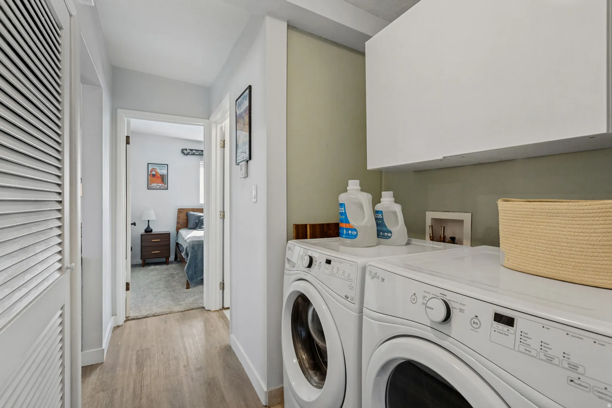 In-unit laundry appliances with overhead cabinetry, wood-finish flooring, and light-toned walls