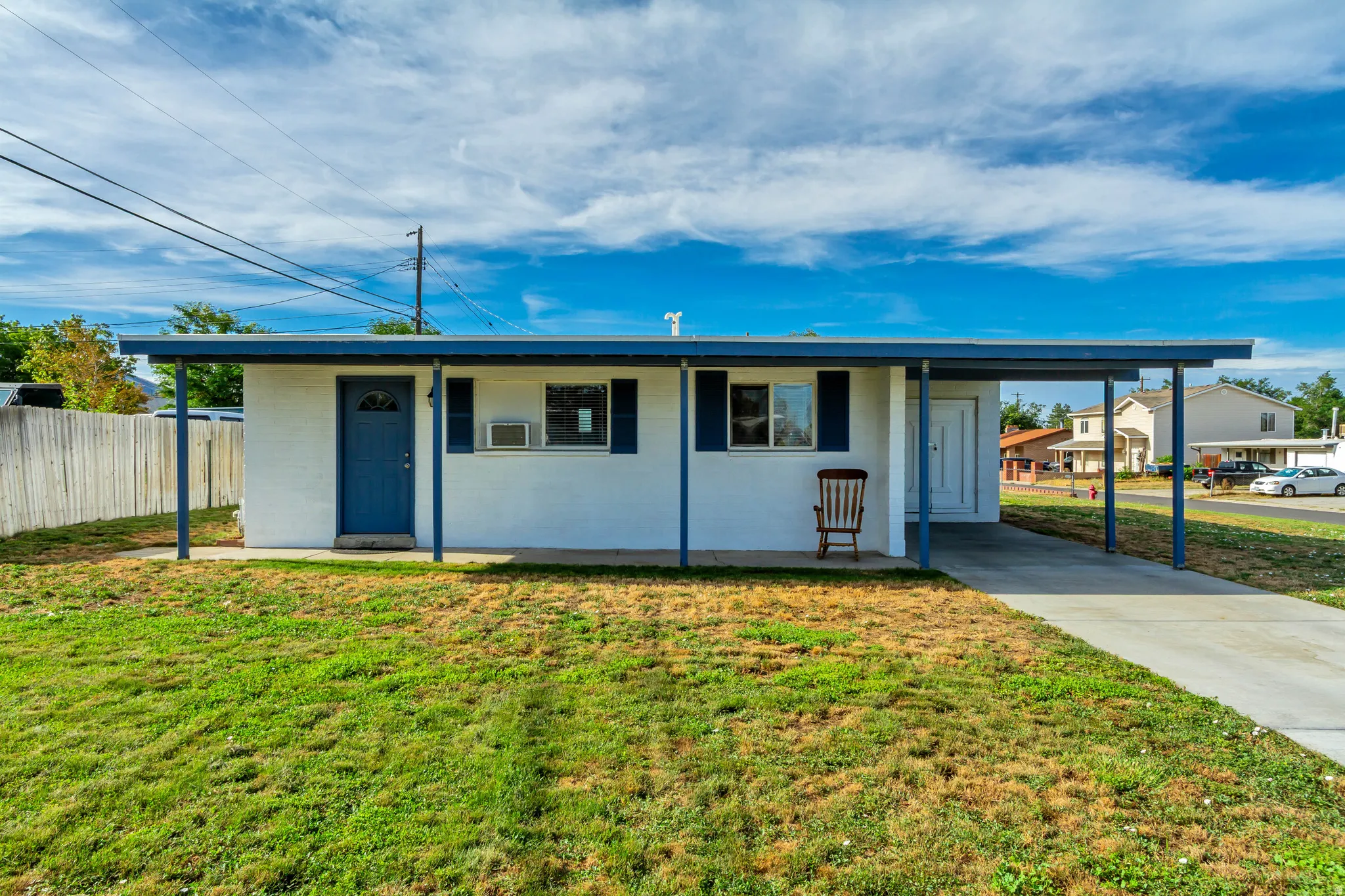 White exterior with blue trim and shutters, covered entryway, and an attached carport