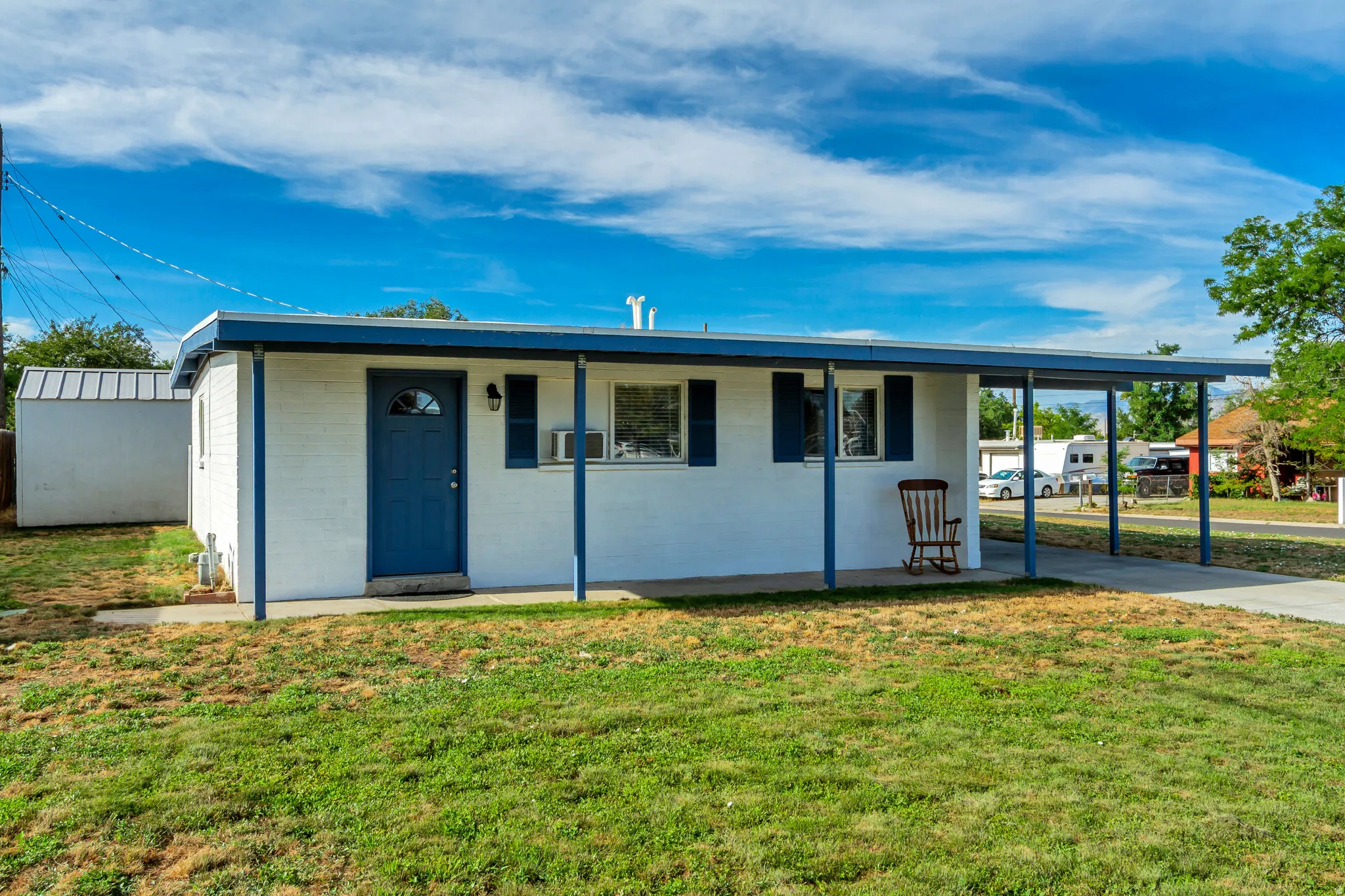 White exterior with blue trim, carport, and shed