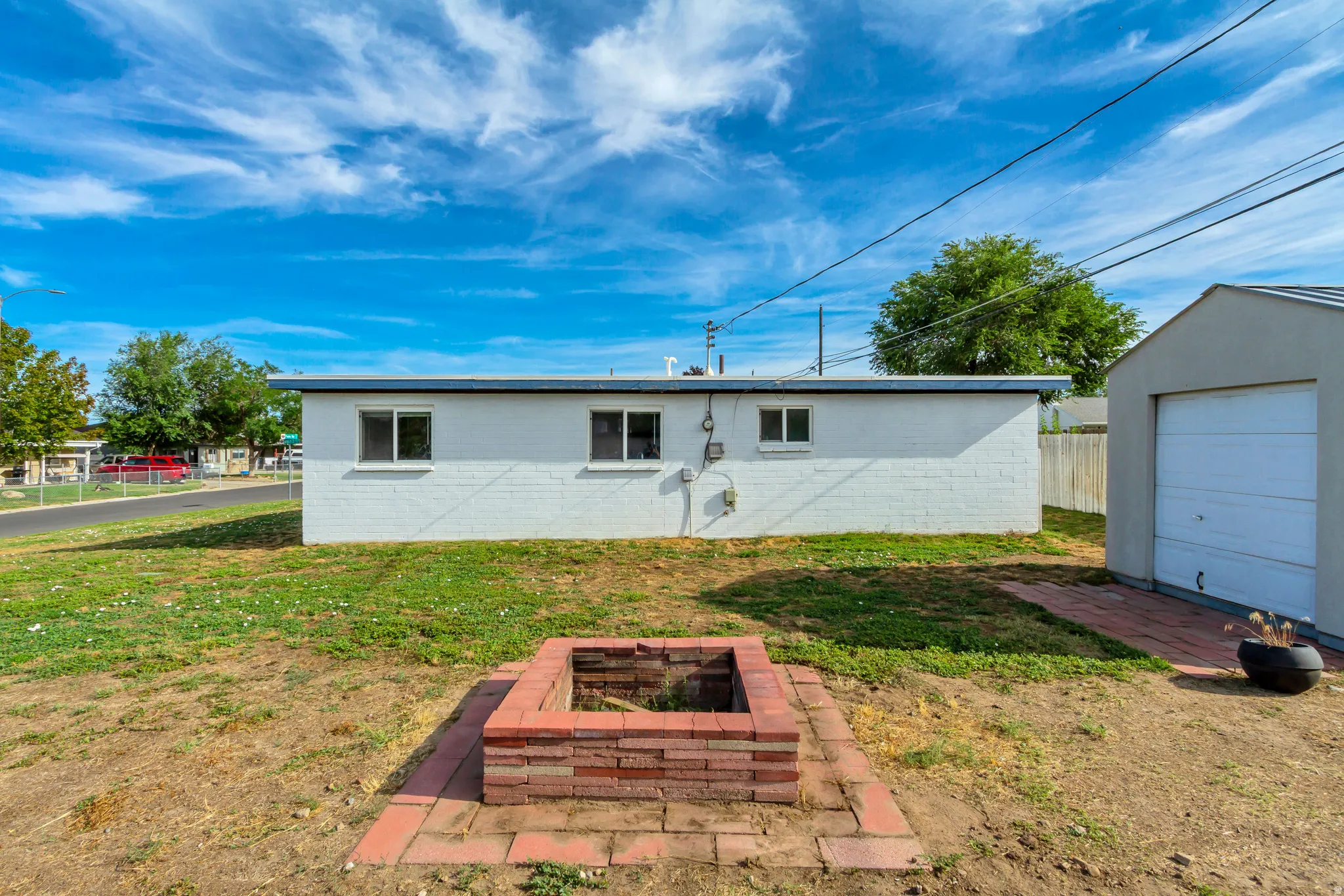 Detached garage with white overhead door, brick fire pit, and low-maintenance exterior