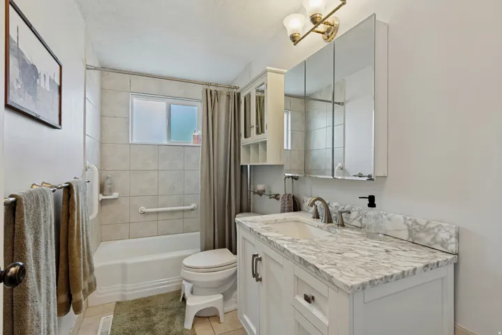 White vanity with a light-toned countertop and integrated sink, dual mirrored medicine cabinet, and a bathtub with tiled surround