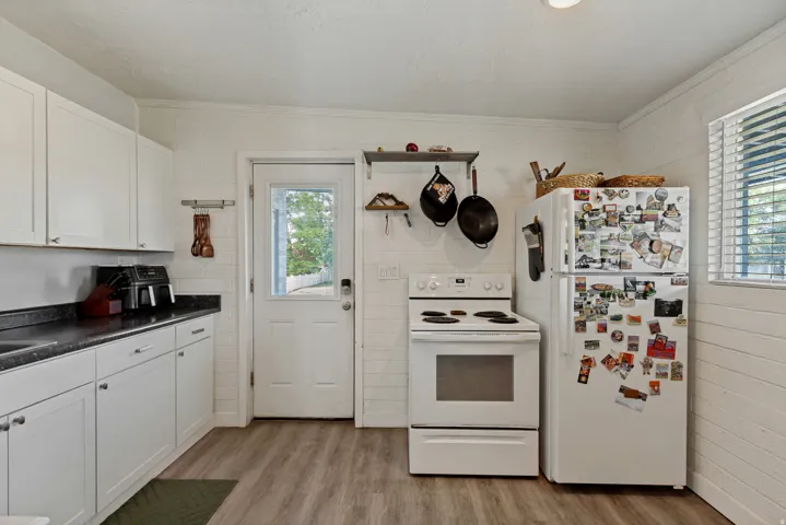 White cabinetry with dark countertops, wood-finish flooring, white appliances, and a glass-paneled door