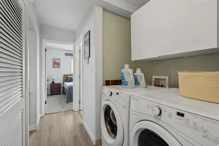 In-unit laundry appliances with overhead cabinetry, wood-finish flooring, and light-toned walls