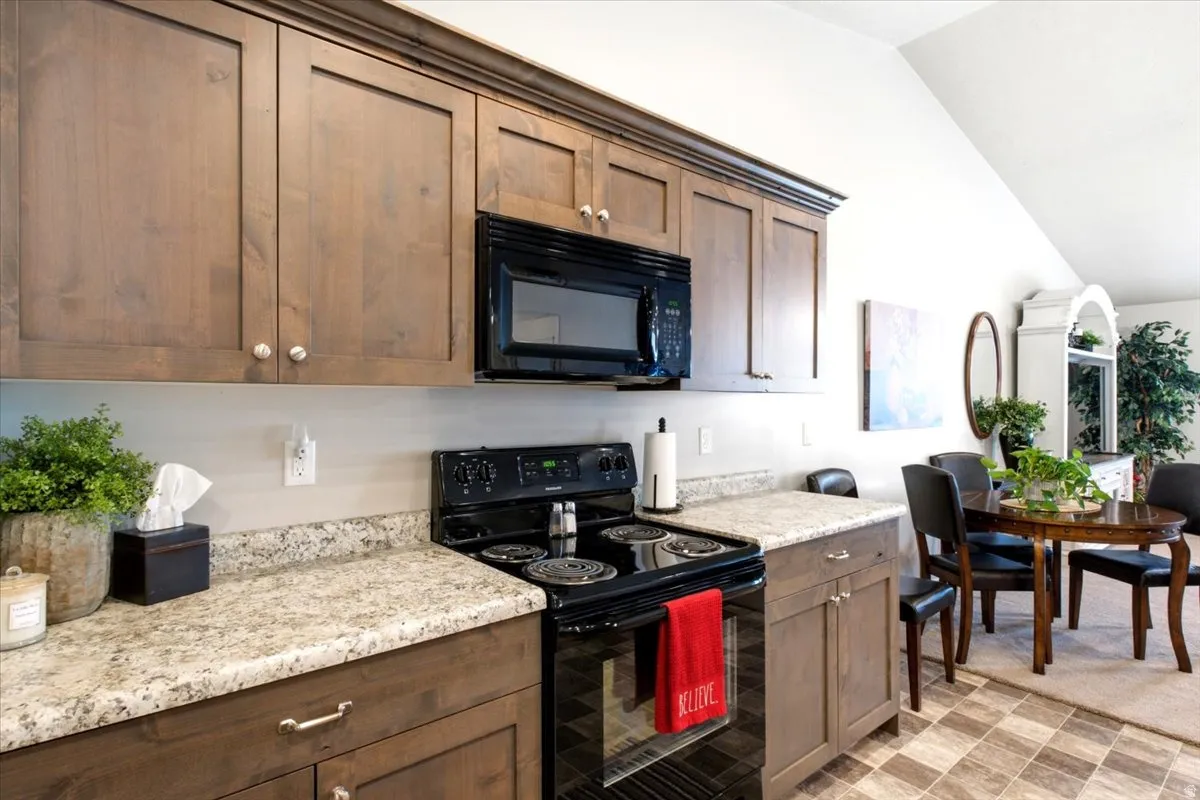 Kitchen featuring wood-finish cabinetry, light-toned countertops, and a black range and microwave
