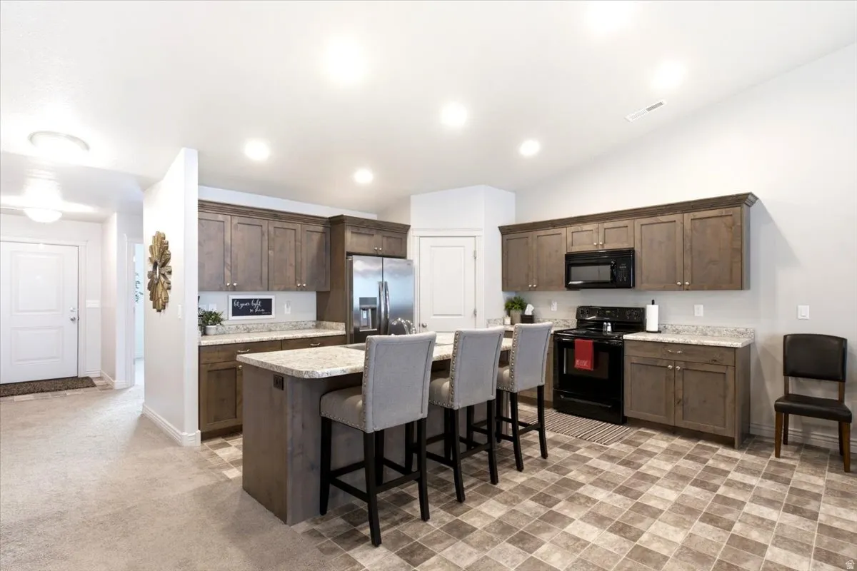 Kitchen featuring an island with stone-finish countertop, dark wood-finish cabinetry, stainless steel refrigerator, and black appliances