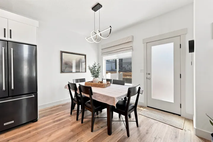 Wood-finish flooring, white cabinetry, modern pendant light fixture, stainless steel refrigerator, and a glass-paned exterior door