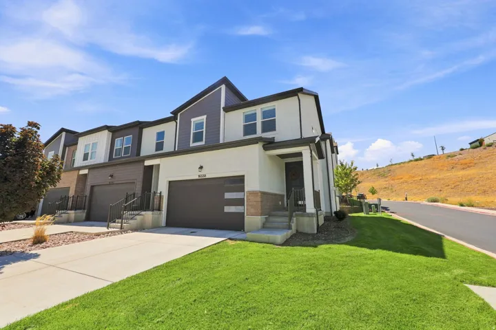 Contemporary townhome facade featuring a two-car garage, stucco and siding exterior, and a manicured lawn