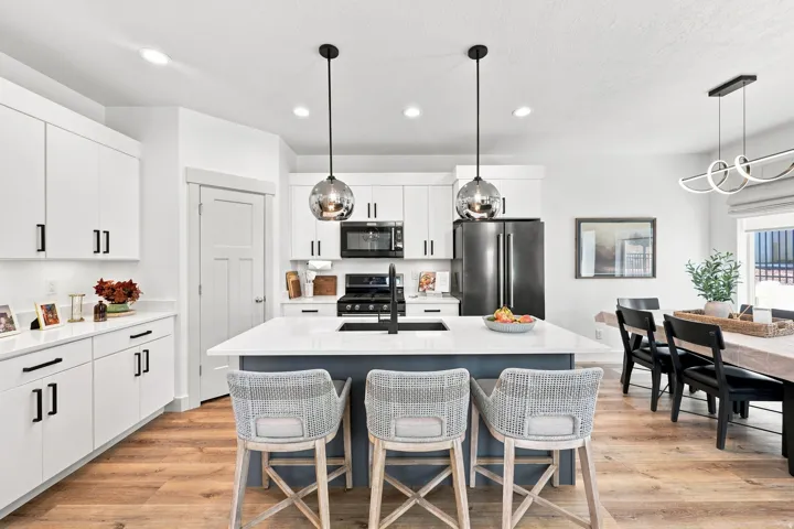 Kitchen featuring white cabinetry, a central island with countertop seating, black appliances, wood-finish flooring, and pendant lighting
