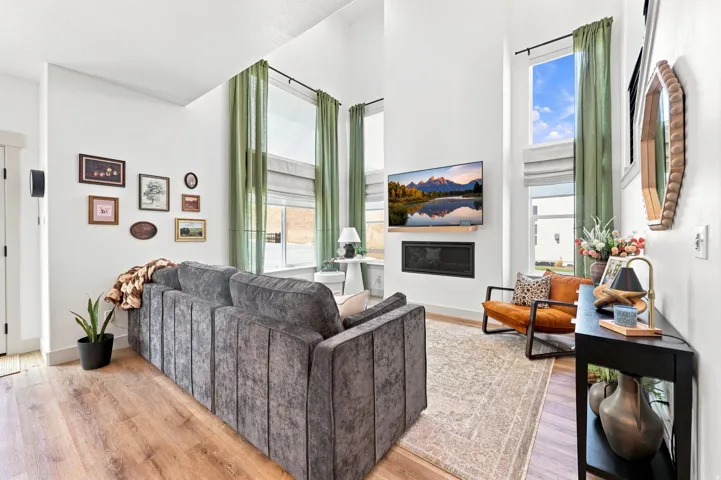 Vaulted ceiling, wood-finish flooring, tall windows, integrated fireplace, and a light color palette