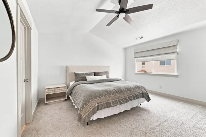 Vaulted ceiling with a contemporary ceiling fan, single window with fabric roman shades, and light-toned wall-to-wall carpeting