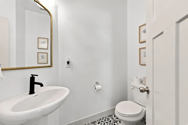 Pedestal sink with a matte black faucet, gold-framed mirror, and patterned floor tile