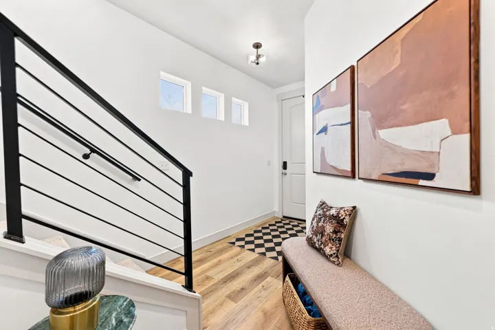 Wood-finish flooring, white walls, black metal staircase railing, checkerboard tile entry, and transom windows