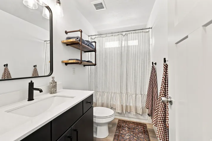 Single vanity with a white countertop and integrated sink, matte black faucet, wall-mounted mirror, and wood-finish flooring