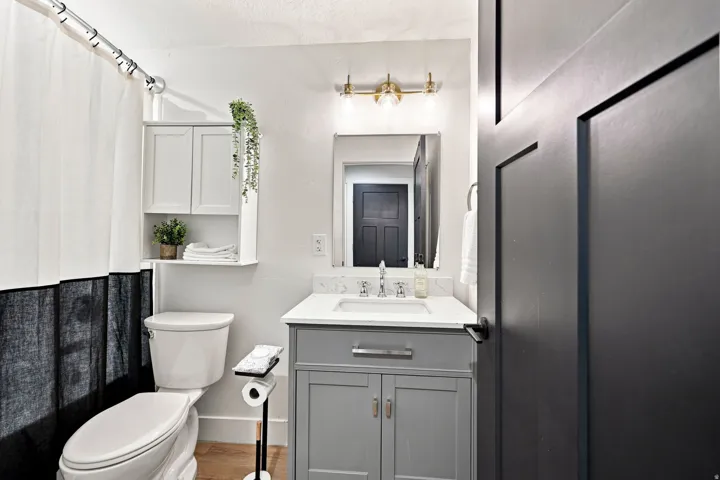 White shaker-style wall cabinet, gray vanity with white countertop, chrome faucet, and gold-finish wall sconce