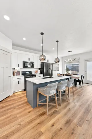 Wood-finish flooring throughout, white cabinetry with dark hardware, kitchen island with integrated sink, recessed lighting, and pendant lighting fixtures