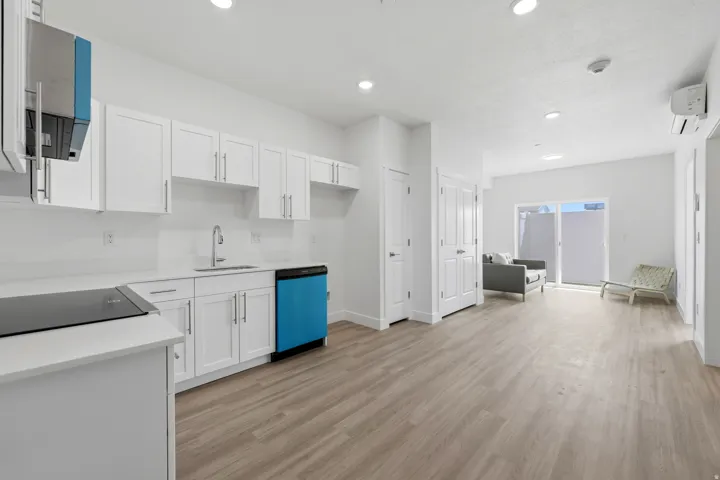 Open-concept space featuring white shaker cabinetry, an integrated cooktop, a built-in dishwasher, light wood-finish flooring, and a sliding glass door