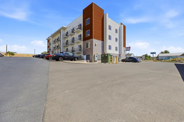 Multi-story building featuring balconies with metal railings, white exterior siding, and brown accent panels
