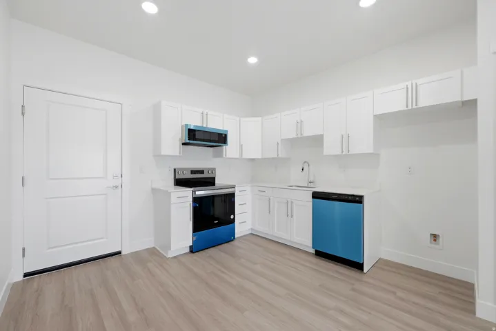 Kitchen featuring white shaker-style cabinetry, a stainless steel sink with a gooseneck faucet, light wood-finish flooring, and recessed lighting