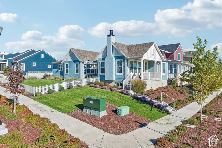 Craftsman-style exterior with vertical siding, exterior stone chimney, covered front porch, and white picket fencing surrounding a landscaped yard
