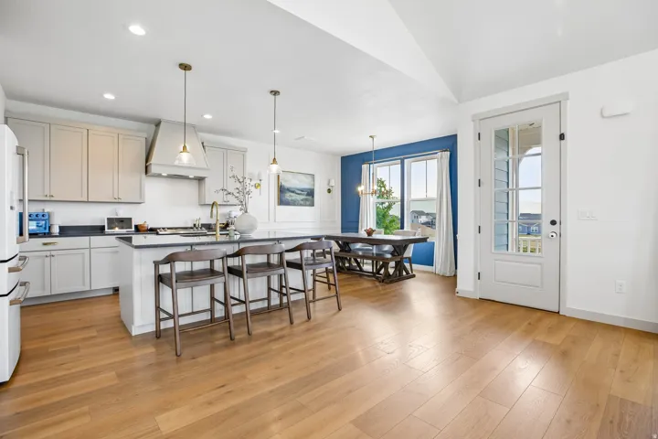 Kitchen featuring a center island with pendant lighting, light wood-finish flooring, white cabinetry, dark countertops, and a white refrigerator