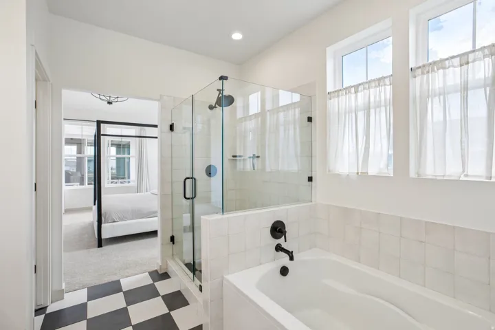 Glass-enclosed shower with matte black fixtures, soaking tub with matte black fixtures, black and white checkered floor tiles, and upper windows