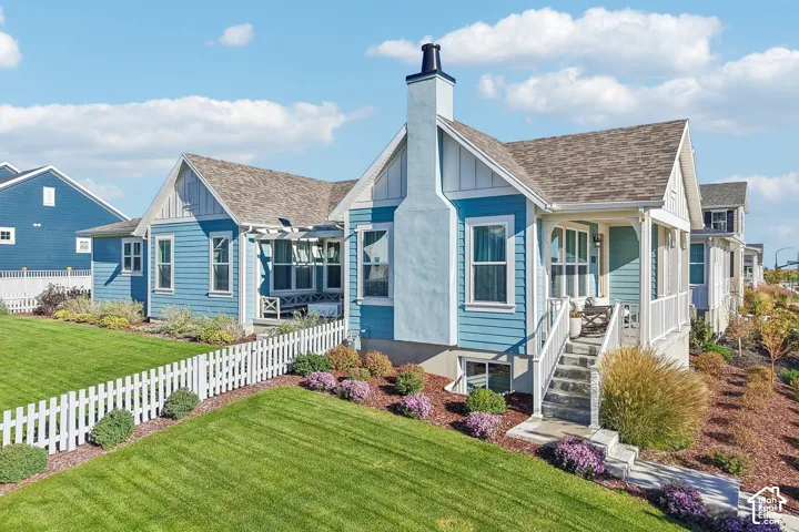 Exterior featuring horizontal lap siding, a prominent chimney, an elevated covered porch with stairs, and a white picket-fenced lawn with landscaped garden beds