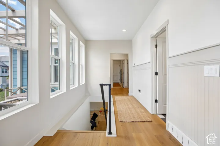 Wood-finish flooring throughout, white paneled walls, multiple windows, and a black metal handrail