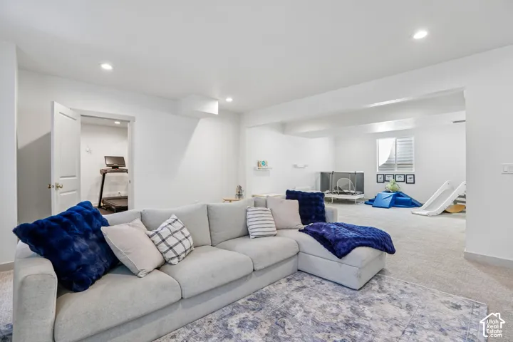 Spacious living area with recessed lighting, light-colored carpeting, a white interior door, and a window with horizontal blinds