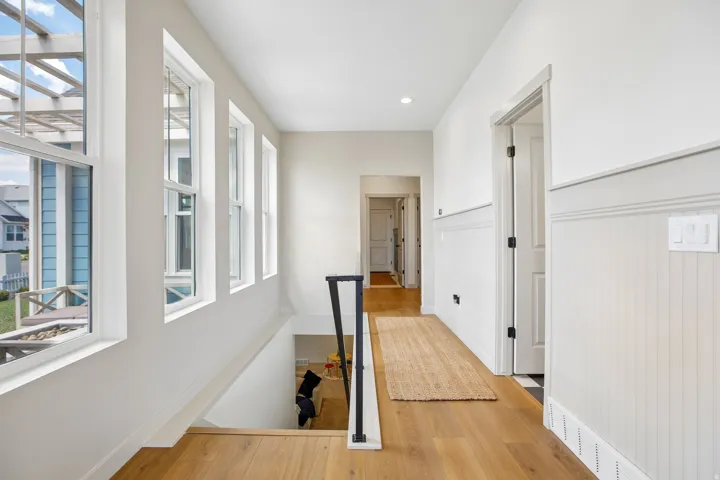 Wood-finish flooring throughout, white paneled walls, multiple windows, and a black metal handrail