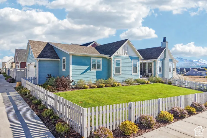 Blue horizontal siding exterior featuring board-and-batten gables, a white picket fence, a manicured lawn, and an exterior chimney