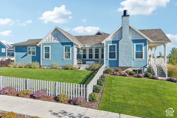 Exterior featuring horizontal siding, a prominent chimney, a covered porch with railings, and a fenced yard with manicured landscaping