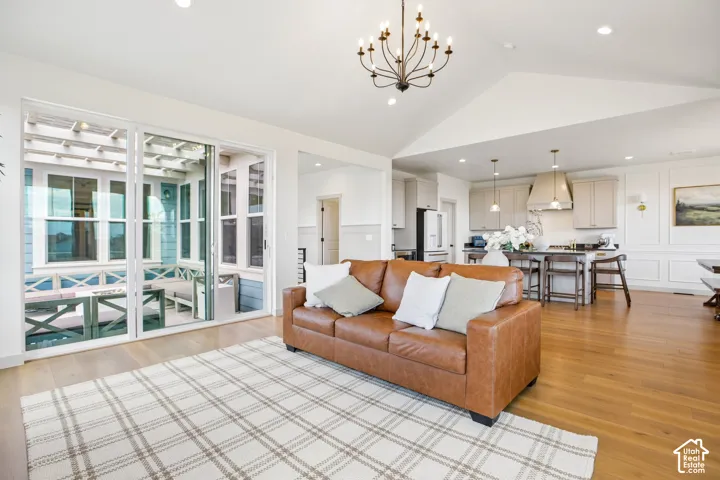 Vaulted ceiling with an iron chandelier, light wood-finish flooring, and white paneled walls