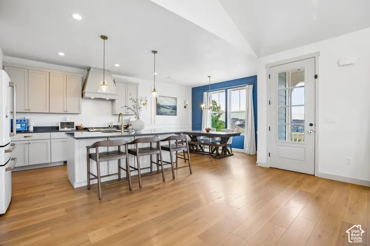 Kitchen featuring a center island with pendant lighting, light wood-finish flooring, white cabinetry, dark countertops, and a white refrigerator