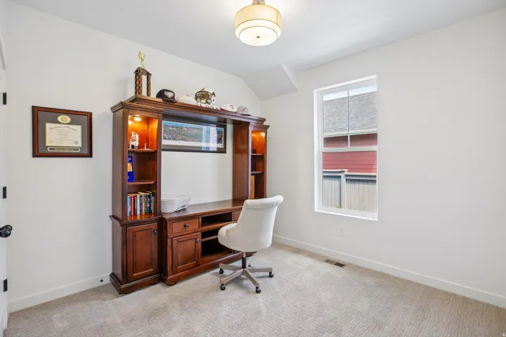 Recessed ceiling fixture, light-toned wall paint, built-in wood-finish shelving and desk unit, single window, and light-toned carpet flooring