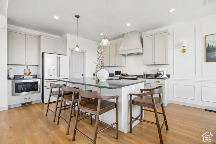 Kitchen featuring a central island with seating, pendant lighting, stainless steel appliances, light-toned cabinetry, and wood-finish flooring