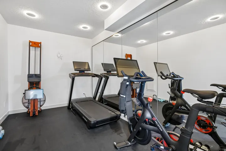 Dedicated fitness area featuring wall-to-wall mirrors, recessed lighting, and durable rubber flooring