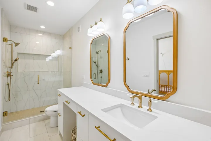 Dual vanity with integrated sinks, gold-finish hardware, and decorative framed mirrors
