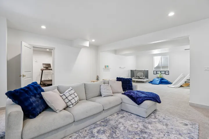 Spacious living area with recessed lighting, light-colored carpeting, a white interior door, and a window with horizontal blinds