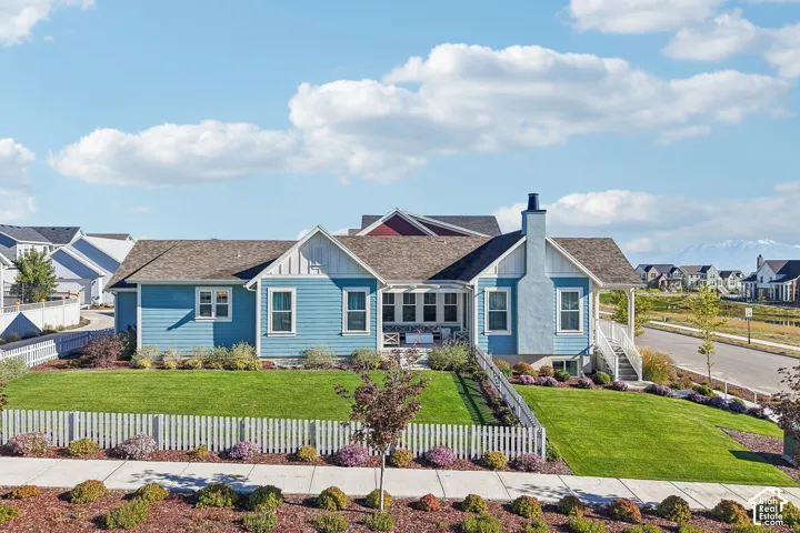Exterior featuring blue lap siding, white trim accents, a chimney, a covered porch, and a white picket fence surrounding a grass lawn