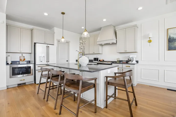 Kitchen featuring a central island with seating, pendant lighting, stainless steel appliances, light-toned cabinetry, and wood-finish flooring