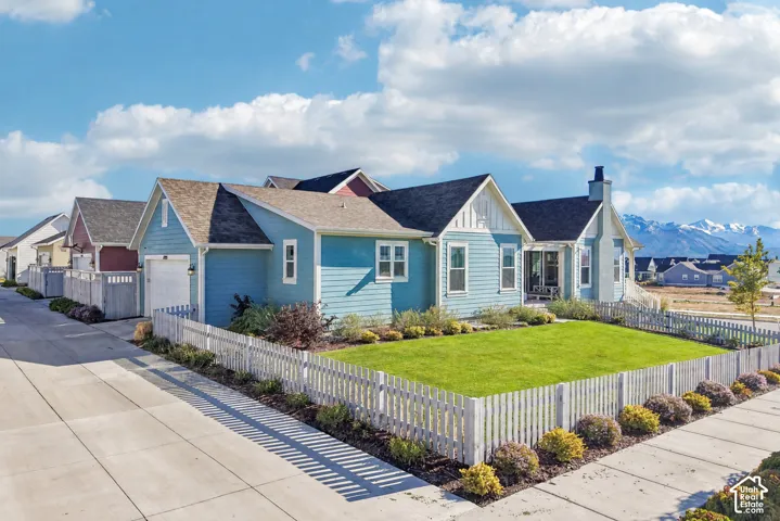 Blue lap-siding exterior featuring a picket fence, gabled rooflines, stone chimney, and mountain backdrop