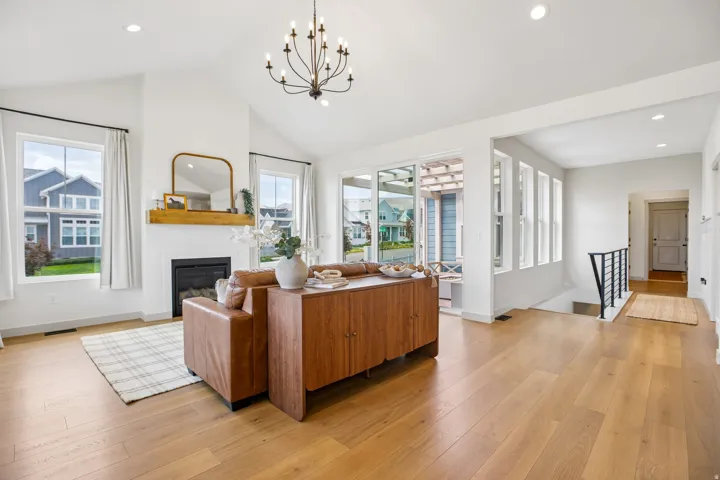 Vaulted ceiling with a chandelier, wood-finish flooring, white fireplace with a wood mantle, multiple windows, and a sliding glass door