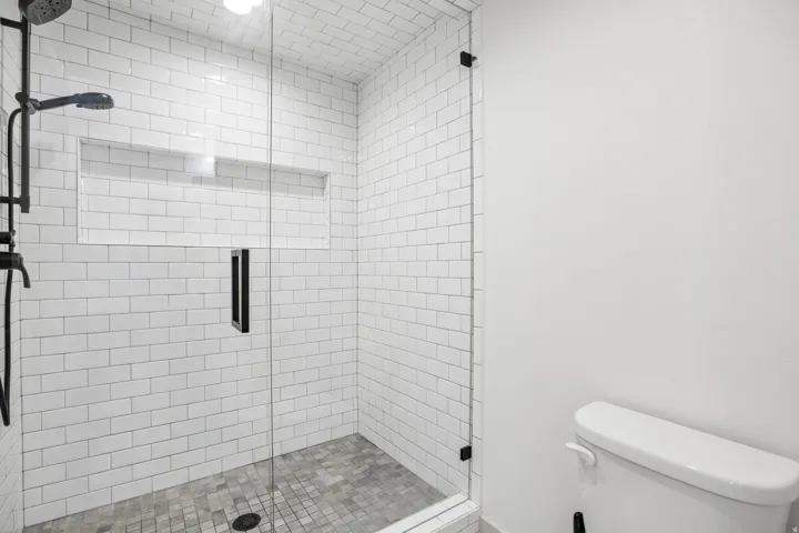 Shower featuring white subway tile surround, recessed shelf, glass enclosure with matte black hardware, and mosaic tile flooring