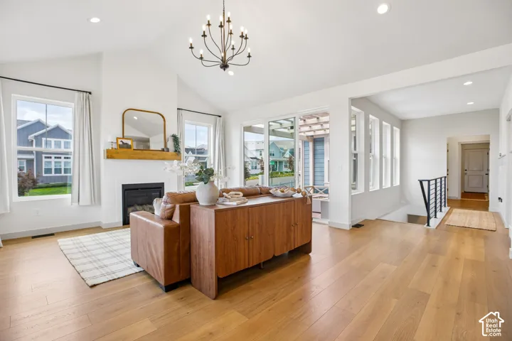 Vaulted ceiling with a chandelier, wood-finish flooring, white fireplace with a wood mantle, multiple windows, and a sliding glass door